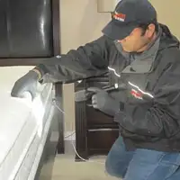 Bed bug inspection technician checking a mattress and bed frame for signs of infestation in Aurora, CO