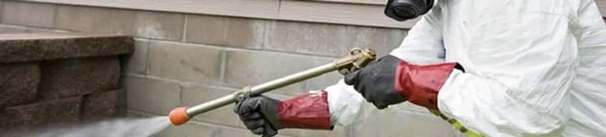 Pest control technician applying exterior insect treatment along a home foundation in Aurora, CO