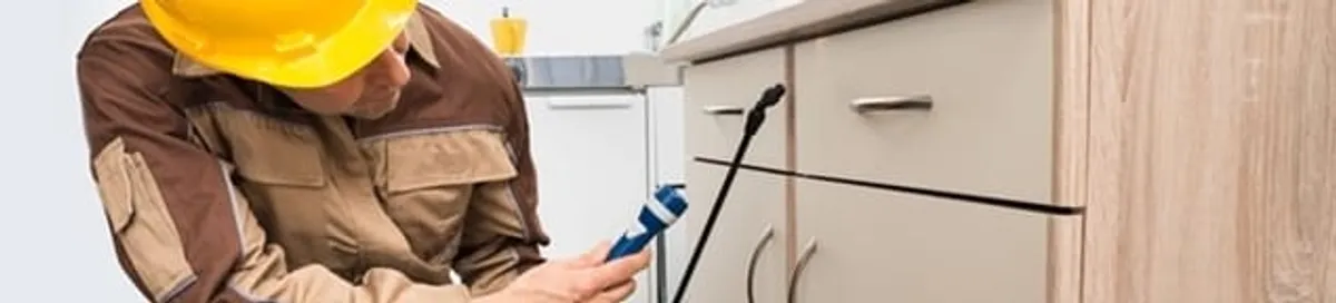 Roach exterminator applying treatment under kitchen cabinets in Aurora, CO