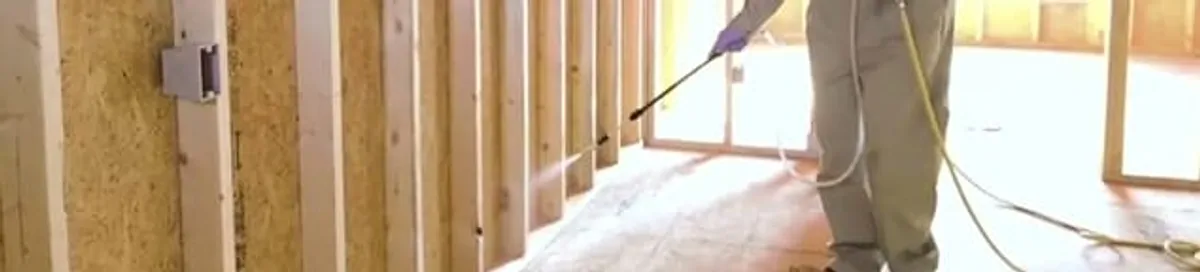 Termite treatment technician applying spray along framing and unfinished walls in Aurora, CO